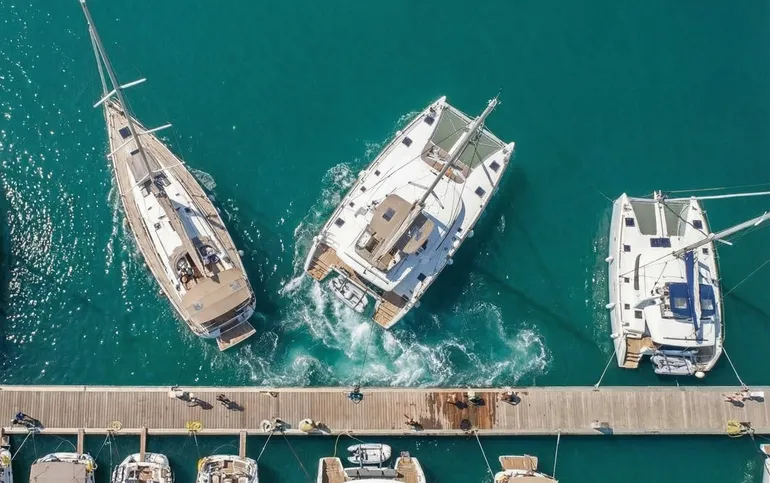 A sailboat and a catamaran leaving a marina pier, seen from above